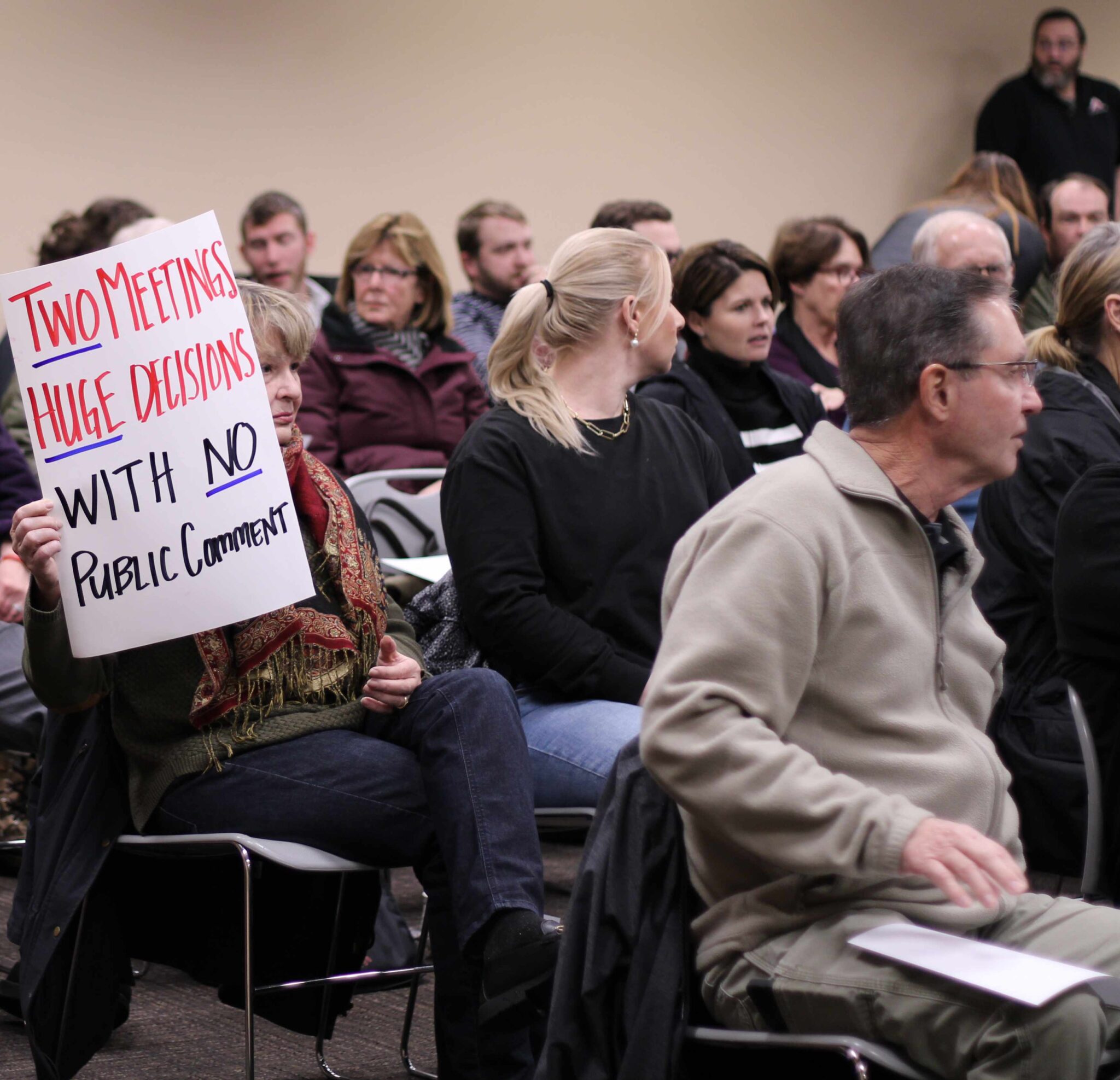 Woman holds up sign "two meetings, Huge decisions, with no public comment